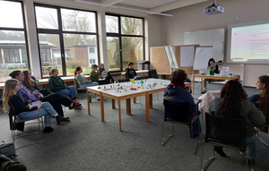 Seminargruppe im Stuhlkreis um einen Tisch mit Playmobil-Figuren